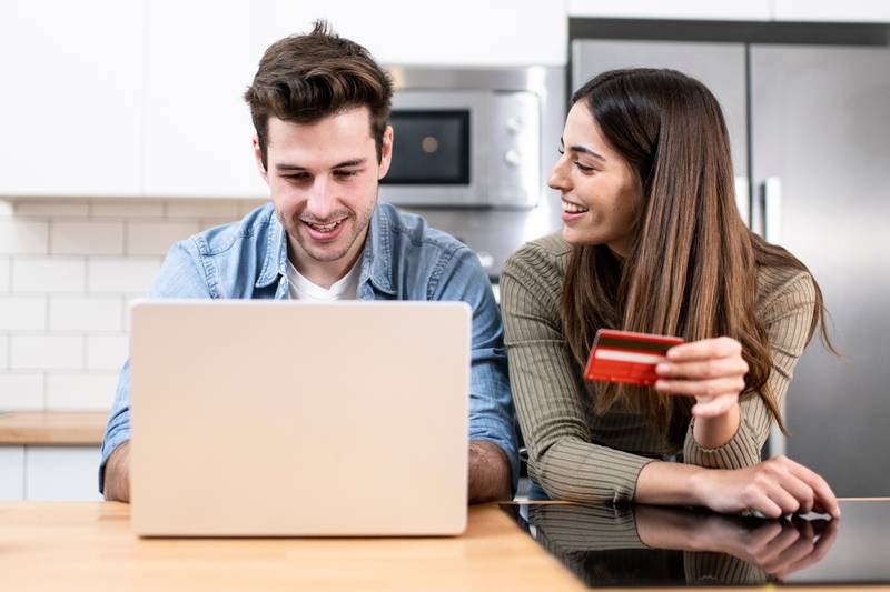 young couple planning vacations together at home looking a laptop. two cheerful young adults sitting on the kitchen. finance concept