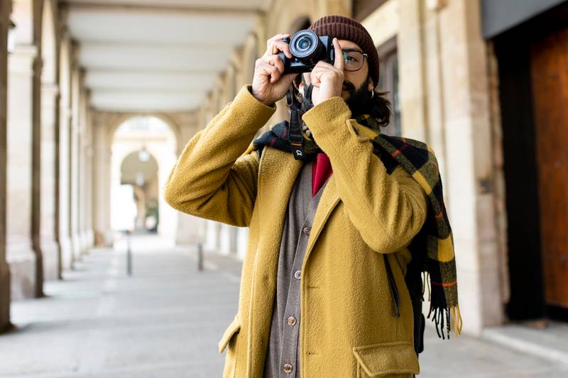 Tourist man taking a photo with his camera in the city. Male photographer having fun on winter vacations on the street
