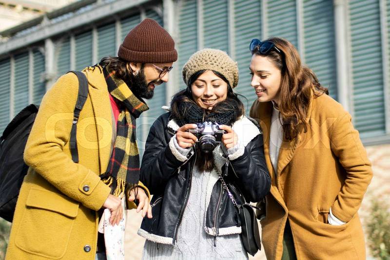 Group of tourists looking a camera on the street. Three cheerful friends taking a photo during a city travel