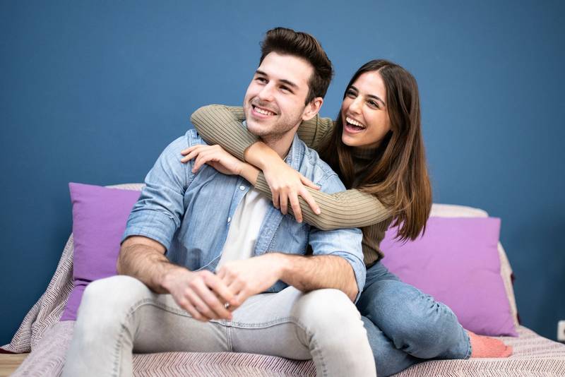 Happy young couple sitting on sofa at home. Portrait of smiling couple looking up