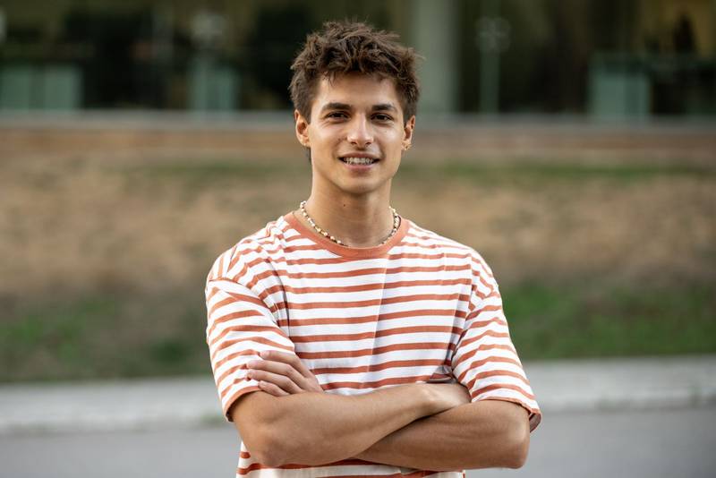 Confident young guy looking at camera with arms crossed.Satisfied teenager standing relaxed outside and smiling.