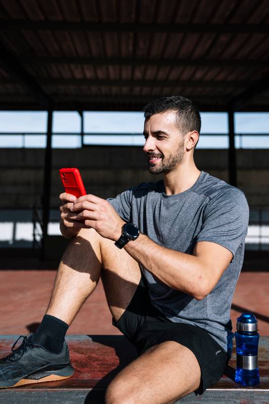 Fit man using smartphone relax resting from exercise in a bench outside. Active sports athlete texting with phone during training.