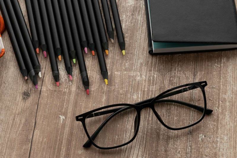 notebook with colored pencils and glasses on a wooden textured table, instruments in workspace