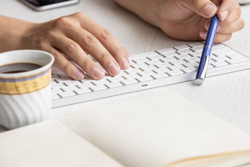 desk with a person's hands holding a pen next to a keyboard, winged a notebook with blank sheets, business in the workplace