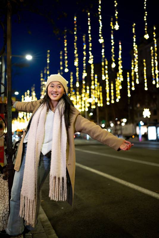 Cheerful young girl enjoying christmas lights in the street. Carefree lady having fun at night in the city during winter.