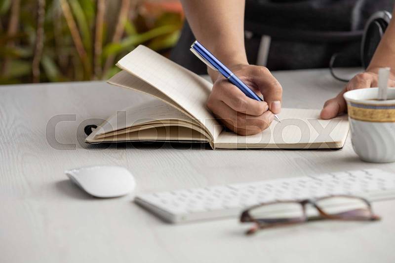 person's hand taking notes with a blue pen on a notebook, workplace