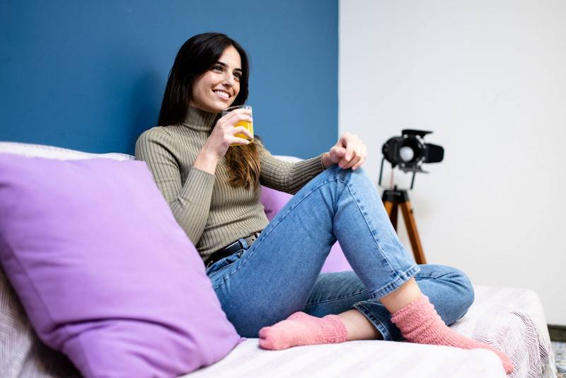 Happy young woman sitting on sofa at home and looking at camera. Portrait of comfortable caucasian woman similing and relaxing on armchair