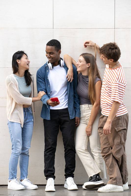 Young diverse group laughing together leaning against a grey wall.Cheerful men and women talking and having fun outside.
