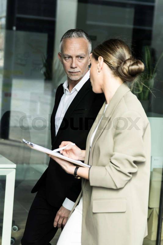 Side view of business people walking and talking in the office. Senior ceo and young executive having a meeting while holding a folder.