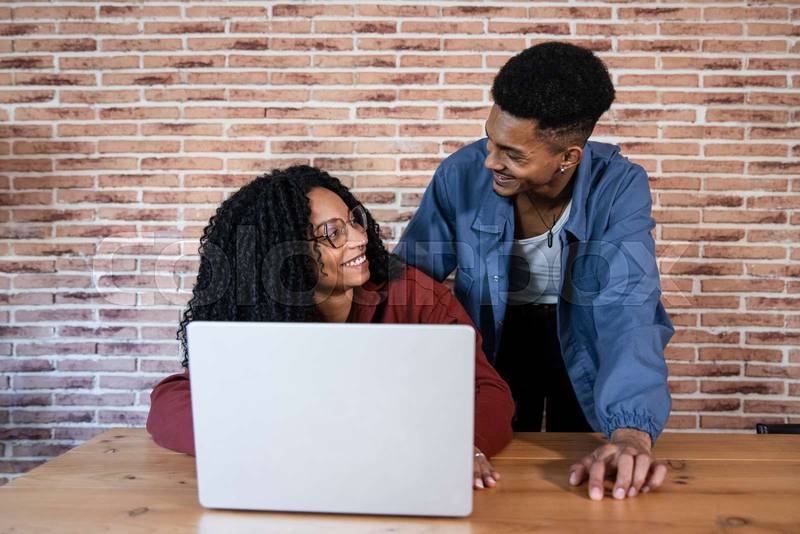 Young couple using laptop in the living room. Satisfied man and woman smiling at each other while using a computer together at home.