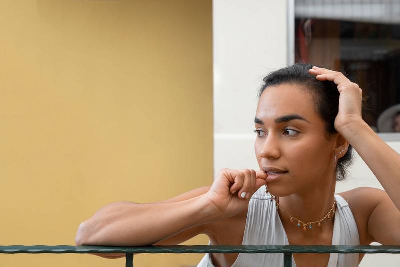 on a balcony a young brunette woman with her hair tied up and wearing a necklace, rests