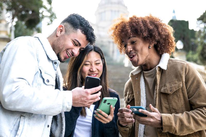 Three young diverse people looking at a smartphone and laughing .Multiracial group having fun and using phones in a park.