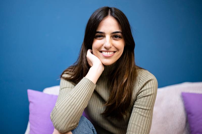 Happy young woman sitting on sofa at home and looking at camera. Portrait of comfortable caucasian woman similing and relaxing on armchair