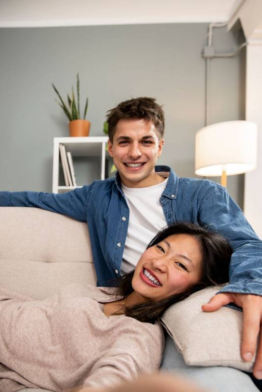 Cozy smiling wife and husband enjoying carefree free weekend time at home taking a picture. Affectionate relaxed couple sitting comfortable at their living room taking a selfie