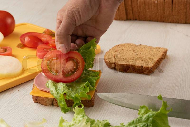 hands preparing and placing fresh vegetables in a sandwich