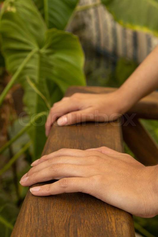 hands of a person approaching a wooden handrail in the background natural leaves of a garden