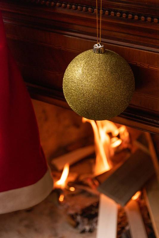 Christmas light bulb of golden color with glitter hanging as decoration in a lit wooden fireplace