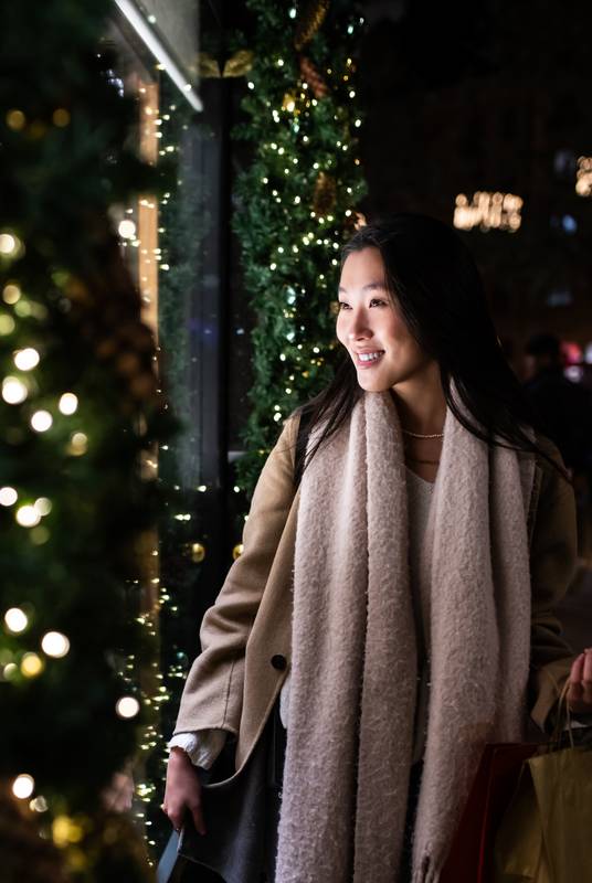 Carefree young lady looking at shop window carrying bags at night. Happy female holding shopping bags in Christmas.