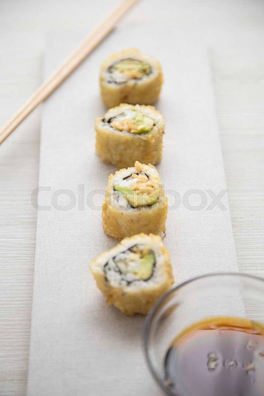 sushi rolls next to a bowl with soy sauce and chopsticks, food