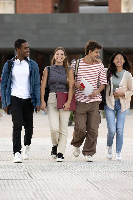 Diverse group of friends walking in the street with folder looking at camera. Multiracial young students smiling staring at camera with confidence and happiness.
