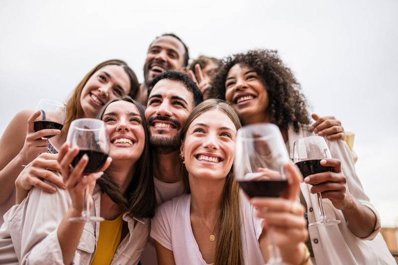 Bottom view of multiracial group of friends having drinks in a rooftop party. Diverse young happy group of millennials drinking wine in a terrace taking a picture.
