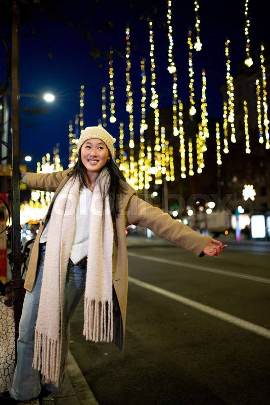 Cheerful young girl enjoying christmas lights in the street. Carefree lady having fun at night in the city during winter.