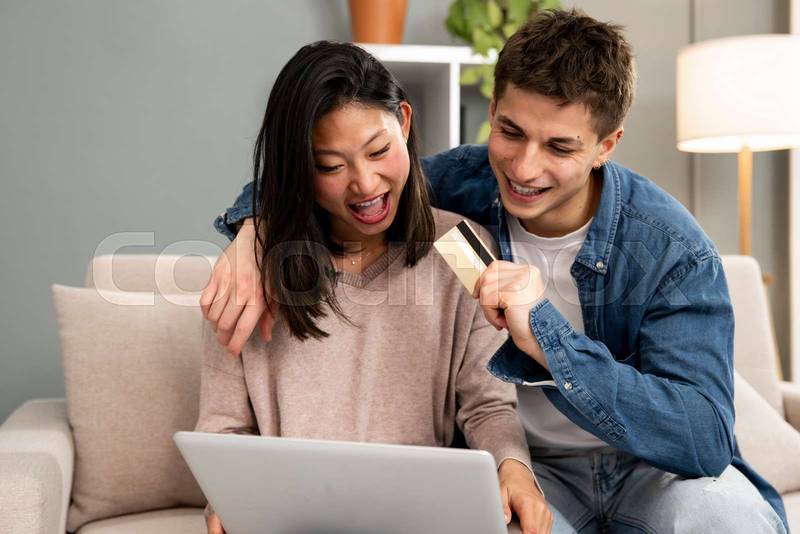 Young carefree diverse couple shopping online with laptop in a sofa. Happy man and woman happy for paying with credit card using a computer at home.