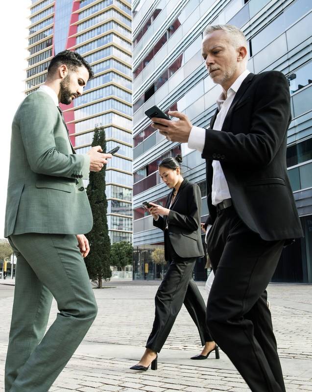 Side view of a group of businessmen and a businesswoman walking in the street while looking at their phones. Multiracial businesspeople checking their phones while waking in the city.