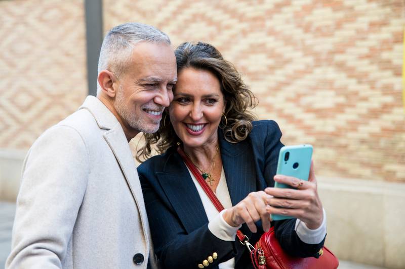 Happy mid adult tourists travelling together using phone together in the street. Lovely mature friends taking picture together while traveling.