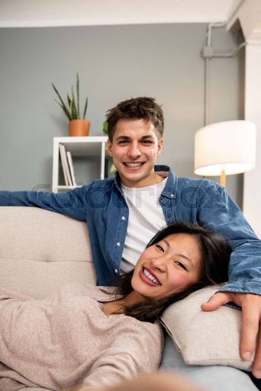 Cozy smiling wife and husband enjoying carefree free weekend time at home taking a picture. Affectionate relaxed couple sitting comfortable at their living room taking a selfie