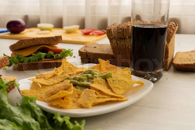 table with a plate of crunchy nachos accompanied by guacamoles, sandwich