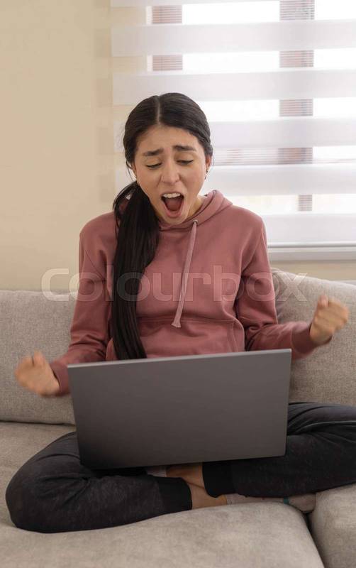 woman yells in frustration while using her laptop on the couch. Concept of digital stress