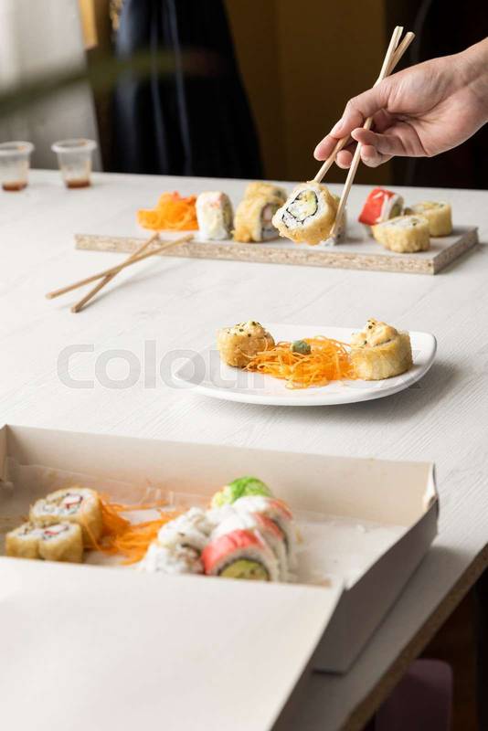 person organizing with chopsticks some sushi roll in a cardboard box and plates on a table in a restaurant food