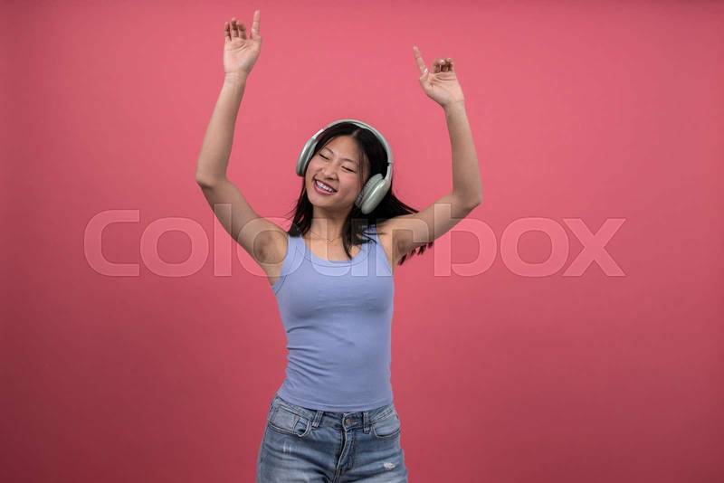 Woman with headphones dancing and raising arms a red background. Isolated young female celebrating listening to music.