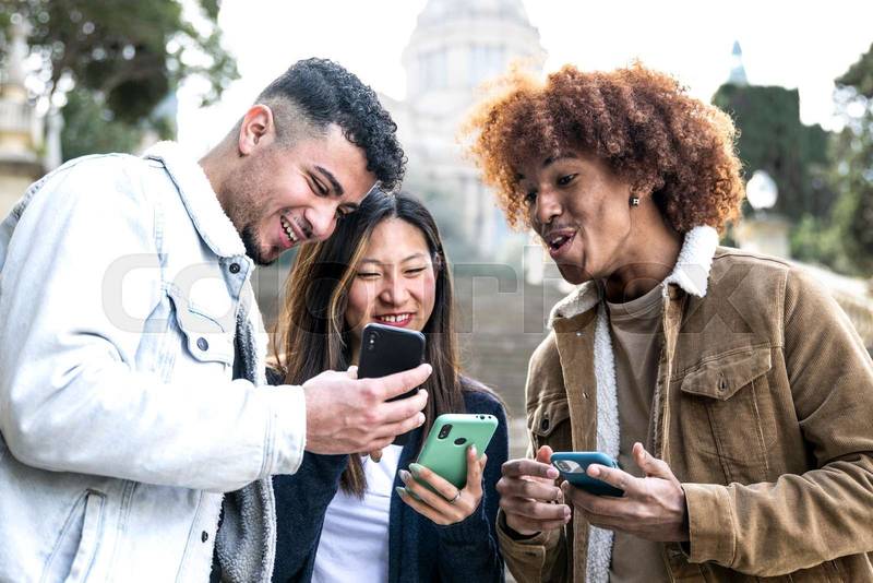 Three young diverse people looking at a smartphone and laughing .Multiracial group having fun and using phones in a park.