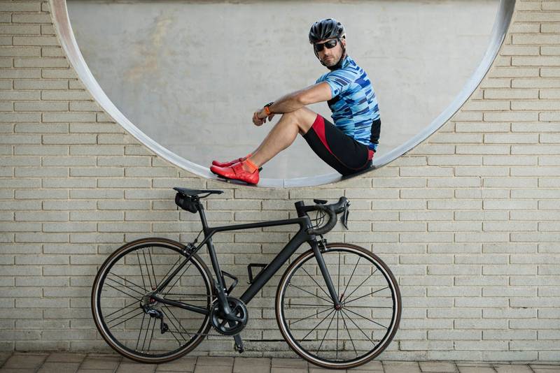 Fit man in sport clothes sitting in a wall with a bike looking at camera. Athletic cyclist resting next to his cycle.