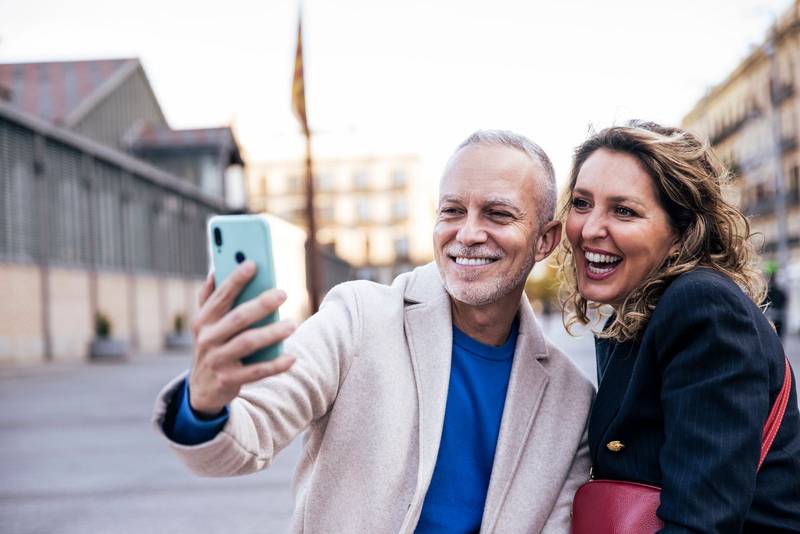 Happy mid adult tourist couple travelling together taking a selfie with her luggage. Affectionate senior husband and wife taking a picture during a weekend romantic trip in european city