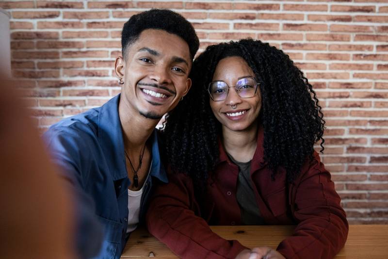 Young carefree relaxed happy couple taking selfie together at modern home. Lovely diverse male and female taking a picture at apartment.