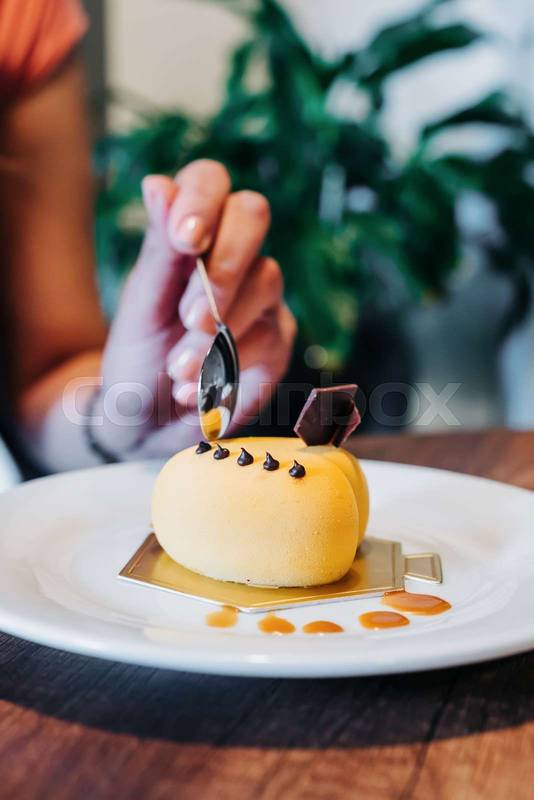 decorated delicious gourmet dessert, person's hand holding spoon and eating the food