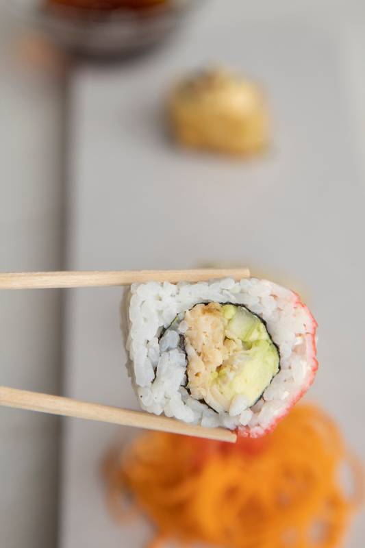 chopsticks holding a sushi roll with rice and seafood, detail of the texture
