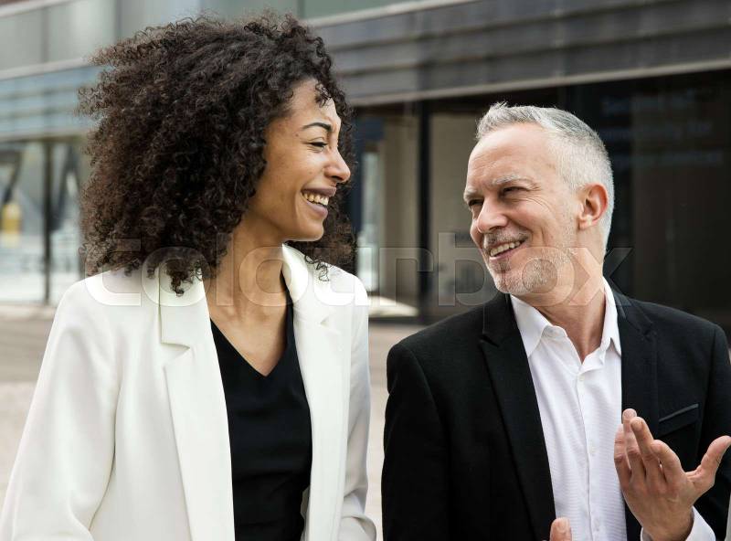 Businesswoman and businessman talking and smiling in the street. Casual meeting between a young executive and a senior ceo having fun outside.