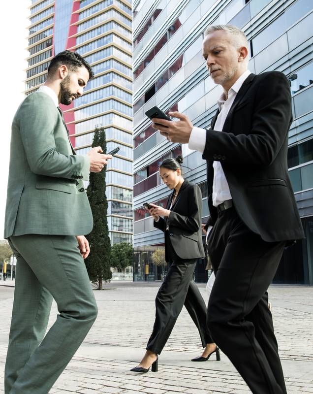 Side view of a group of businessmen and a businesswoman walking in the street while looking at their phones. Multiracial businesspeople checking their phones while waking in the city.
