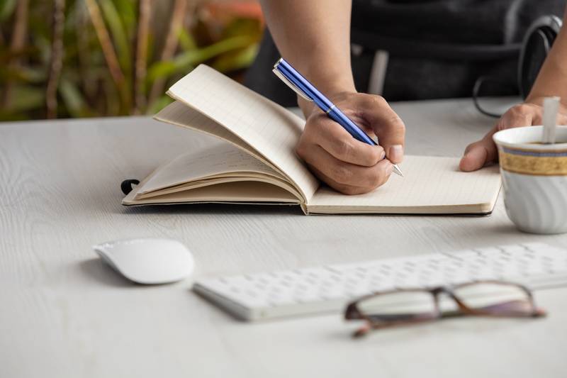 person's hand taking notes with a blue pen on a notebook, workplace