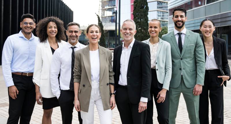 Laughing group of multiethnic businessman and businesswoman looking at camera. Multiracial happy and confident executive team standing in the street.