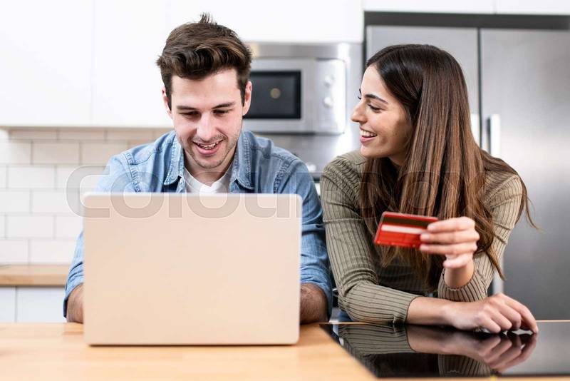 young couple planning vacations together at home looking a laptop. two cheerful young adults sitting on the kitchen. finance concept