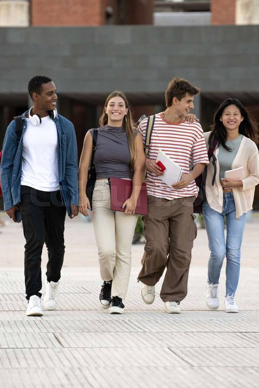Diverse group of friends walking in the street with folder looking at camera. Multiracial young students smiling staring at camera with confidence and happiness.