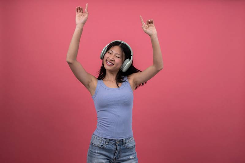 Woman with headphones dancing and raising arms a red background. Isolated young female celebrating listening to music.