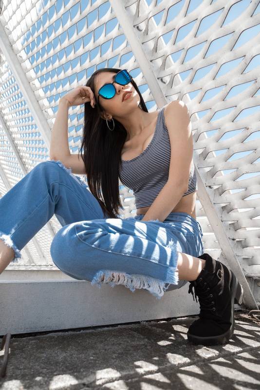 resting in the shade of a structure, beautiful young latin woman with black straight hair sitting posing, wearing fashionable sunglasses