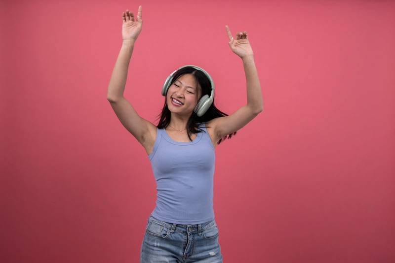 Woman with headphones dancing and raising arms a red background. Isolated young female celebrating listening to music.