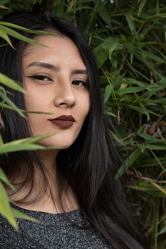 face of a young latin woman wearing makeup and with straight black hair and nature